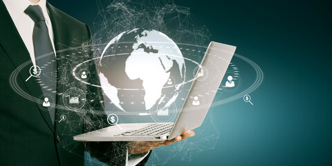 Poster - Close up of businessman hand holding laptop with glowing social globe hologram on blue background. Information, data and communication concept.