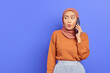 © Bangun Stock Photo - Cute beautiful asian woman in brown sweater and hijab talking on mobile while looking sideways isolated over purple background. People islam religious concept
