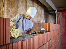 Smiling Bricklayer Applying Cement On Bricks Working At Construction Site