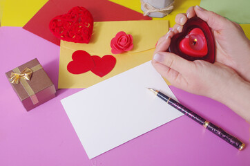 Poster - Love letter. Envelopes, gift box, red hearts, hands holding a candle on a colored background. Place for an inscription. 