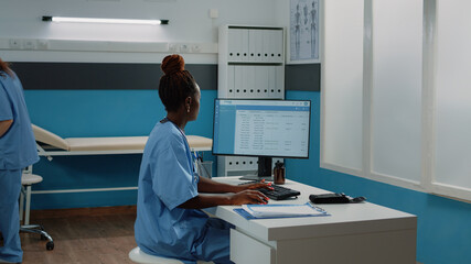 Wall Mural - Medical assistant typing on computer keyboard in cabinet. Woman working as nurse with uniform using monitor for checkup appointments and healthcare practice while sitting as desk.