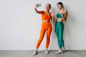 Two young women meet at gym, making selfie photo while standing together at gym