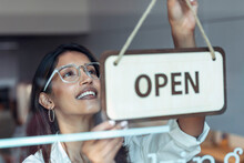 Smiling young businesswoman hanging open sign at entrance of coworking office