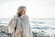 © Westend61 - Smiling blond woman wrapped in blanket at beach