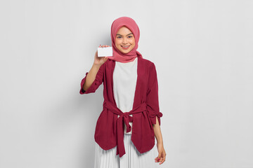 Poster - Cheerful beautiful Asian woman in casual shirt and hijab showing credit card isolated over white background. People religious lifestyle concept