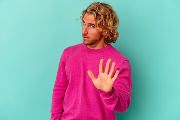 Wall Mural - Young caucasian man isolated on blue background rejecting someone showing a gesture of disgust.