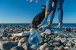 Close-up of a volunteer woman collecting plastic, foam on a pebble beach in a black garbage bag, copy space. Concept of garbage-free seas, ecology.