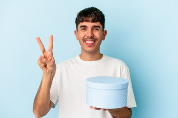 Young mixed race man holding a box present isolated on blue background showing number two with fingers.