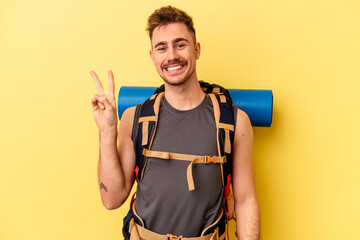 Young hiker caucasian man isolated on yellow background joyful and carefree showing a peace symbol with fingers.