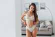 © standret - Standing against sofa. Beautiful woman in underwear is posing indoors