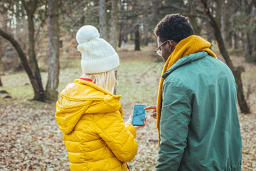 A happy young couple in love with friends of travelers dressed in a casual style using a mobile phone in the woods of a nature park. They try to use navigation to find the desired location