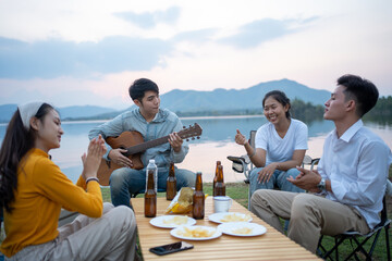 Wall Mural - happy group of Asian friends Play guitar and sing enjoying camping and drinking beer