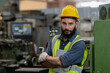 © eakgrungenerd - Portrait of man engineer wear yellow helmet crossed arms with tablet and uniform standing at industrial workshop. handsome workman with beard on face ​in factory. Copy space.
