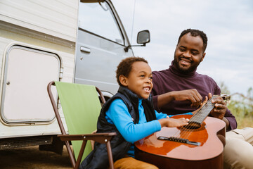 Wall Mural - Black man teaching his son to play guitar during journey on trailer