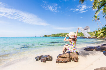 Young Asian lady tourist sitting on the  rock  in to the beach  on her holiday.