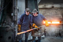 Engineer With Apprentice Inspecting A Forged Steel Part In Industrial Forge