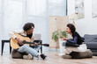 © LIGHTFIELD STUDIOS - Cheerful african american woman with synthesizer talking to boyfriend with acoustic guitar at home.