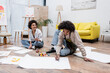 © LIGHTFIELD STUDIOS - African american man painting on floor near smiling girlfriend and paints at home.
