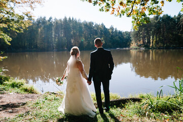 Wall Mural - Wedding moment, couple of newlyweds looking at lake, on nature in the park. Wedding ceremony near lake.