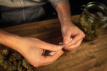 Wall Mural - Man rolling marijuana cannabis joint in coffee shop Amsterdam with CBD weed buds in glass jars.