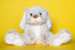 Stuffed soft toy bunny on yellow background. Easter concept. Beautiful white toy bunny sitting on colored background.