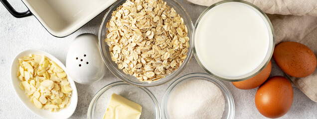 Wall Mural -  Ingredients for pudding or oatmeal pie on a light gray culinary background. Eggs, cereals, almonds, sugar, milk and butter on the kitchen table. Top view. Banner