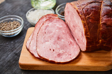 Wall Mural - Homemade ham, sliced on a wooden table on a cutting board with spices and salt. Traditional ham homemade, ready to eat, delicious breakfast. The concept of meat products.