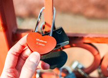 Closeup Person Hand Holding Heart Shape Padlock With Word At The Red Bridge, Depth Of Field. Traditional Symbol For Strengthen, Loyalty And Eternity Love Of Couple. Romantic Engagement Message Concept