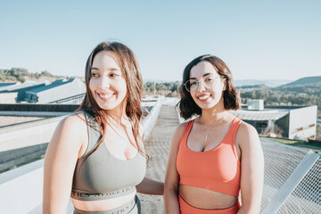 Portrait of two young sporty girls smiling to camera before starting to train. Working out clothes, top and leggings, African woman fitness. Sunset ambient, slim bodies.