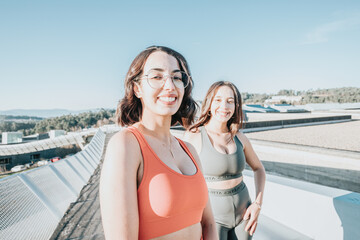 Portrait of two young sporty girls smiling to camera before starting to train. Working out clothes, top and leggings, African woman fitness. Sunset ambient, slim bodies.