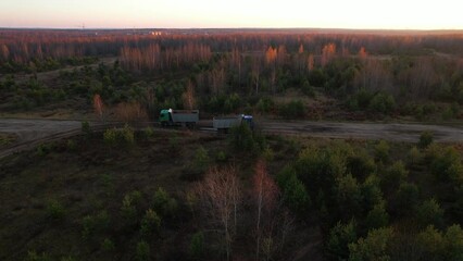 Wall Mural - Dump truck driving on a forest road through a forest with trees during sunset. Dump truck transported sand from the open pit.  Arial view of the opencast mine. 