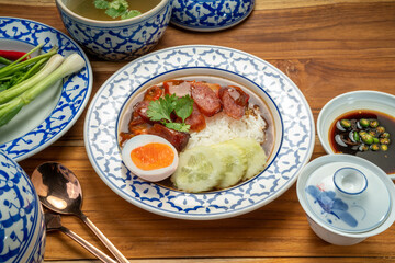 Wall Mural - Rice with red roasted pork with sauce and Egg topped in a white dish on wooden table.