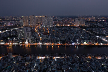 Wall Mural - Panoramic view drone shot of Ho Chi Minh City in late evening looking across the Kenh Te canal with reflections and illuminated buildings.