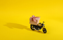 Toy Motorcycle With Gift Box On A Yellow Background With A Shadow. Minimal Holiday Layout