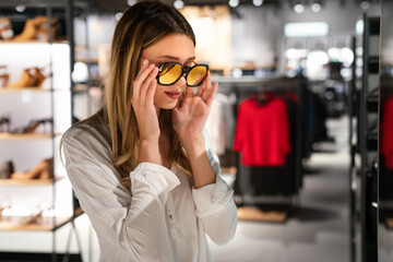 Wall Mural - Portrait of beautiful young woman choosing sunglasses in store. Shopping people fashion concept