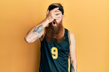 Sticker - Redhead man with long beard wearing basketball uniform peeking in shock covering face and eyes with hand, looking through fingers with embarrassed expression.