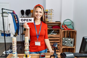 Canvas Print - Young caucasian woman holding banner with open text at retail shop looking positive and happy standing and smiling with a confident smile showing teeth