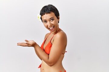 Sticker - Young hispanic woman with short hair wearing bikini pointing aside with hands open palms showing copy space, presenting advertisement smiling excited happy