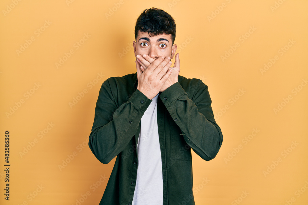 Young hispanic man wearing casual clothes shocked covering mouth with hands for mistake. secret concept.