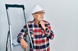 © Krakenimages.com - Handsome mature handyman close to construction stairs wearing hardhat with hand on chin thinking about question, pensive expression. smiling with thoughtful face. doubt concept.