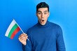 Handsome hispanic man holding bulgarian flag scared and amazed with open mouth for surprise, disbelief face