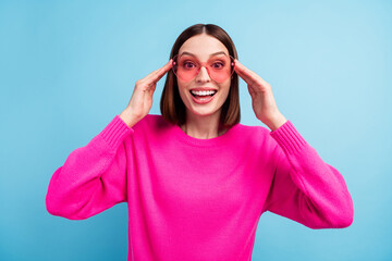 Wall Mural - Photo of impressed funky young woman dressed pink sweater arms heart glasses smiling isolated blue color background