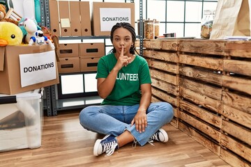 Sticker - Young african american woman wearing volunteer t shirt at donations stand asking to be quiet with finger on lips. silence and secret concept.