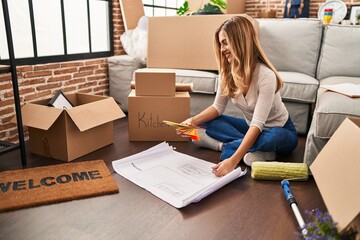 Canvas Print - Young blonde woman sittng on the floor choosing paint color at new home