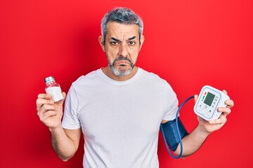 Poster - Handsome middle age man with grey hair using blood pressure monitor holding salt depressed and worry for distress, crying angry and afraid. sad expression.