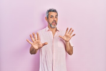 Canvas Print - Handsome middle age man with grey hair wearing casual shirt afraid and terrified with fear expression stop gesture with hands, shouting in shock. panic concept.