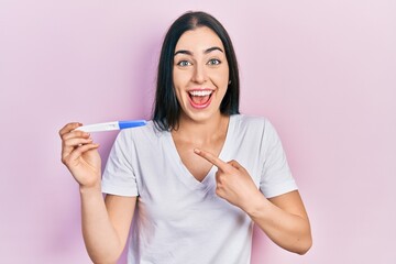 Canvas Print - Beautiful woman with blue eyes holding pregnancy test result smiling happy pointing with hand and finger