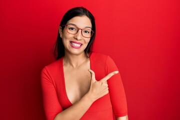 Poster - Young latin woman wearing casual clothes and glasses cheerful with a smile of face pointing with hand and finger up to the side with happy and natural expression on face