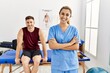 © Krakenimages.com - Young hispanic physioterapist woman smiling happy standing with arms crossed gesture at the clinic