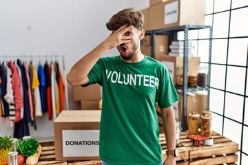 Poster - Young arab man wearing volunteer t shirt at donations stand peeking in shock covering face and eyes with hand, looking through fingers with embarrassed expression.